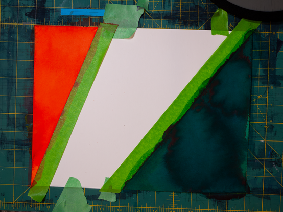 top down view of a piece of watercolour paper with painters tape masked out and sections filled in with vivid orange and green inks.