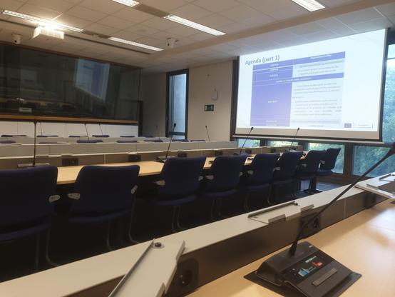 Empty European Commission conference room with large screen showing the agenda of today's meeting.
