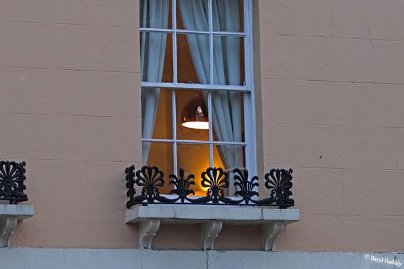 A lamp through a tall period window, at dusk.