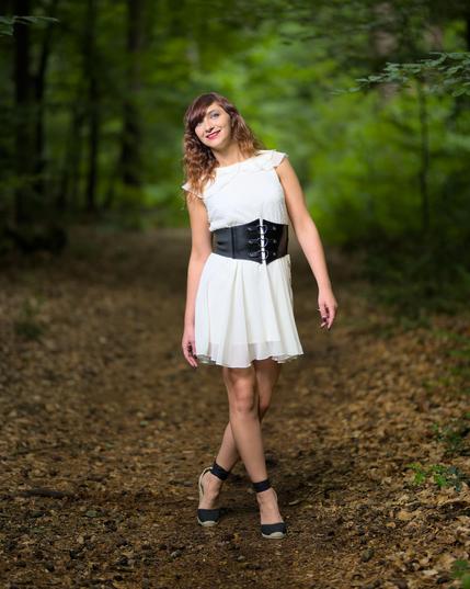 a woman in a white dress is standing on a forest path.