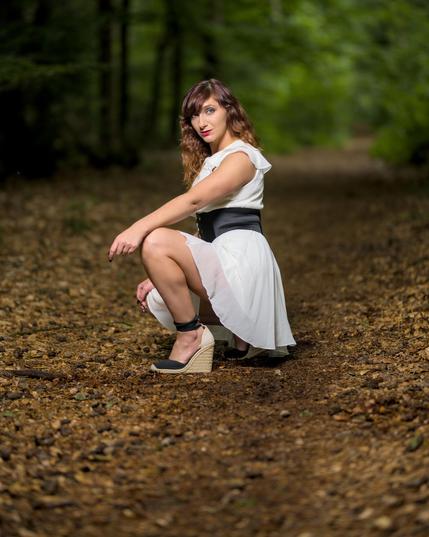 a woman in a white dress is kneeing on a forest path