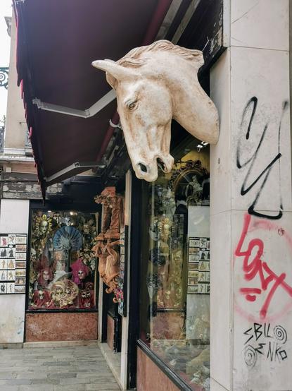 Ein Geschenkeladen in Venedig. An einer Mauer neben dem Schaufenster hängt die Skulptur eines Pferdekopfes.