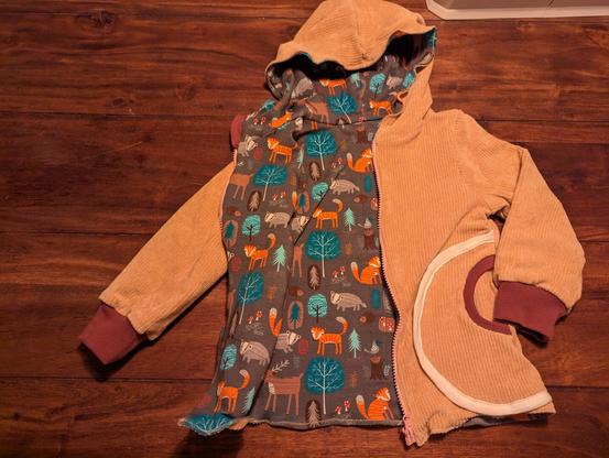 Eine selbstgenähte Kinderjacke aus lachsfarbenden Cord außenstoff. Einem kindlichen Tiermotivjersey als Futterstoff. Beerenfarbenen Bühndchen und ausgesetzten Taschen