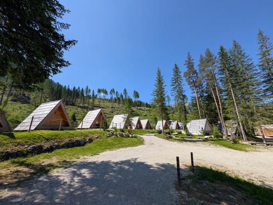 Kleine Holzhütten auf dem Campingplatz vor lichtem Pinien-Bergwäldchen.