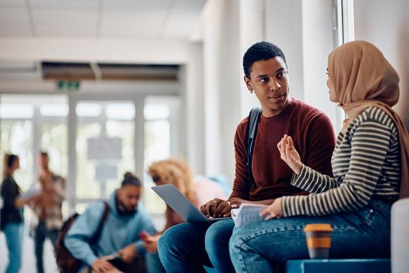 Zwei Jugendliche mit Migrationshintergrund unterhalten sich im Flur einer Schule.