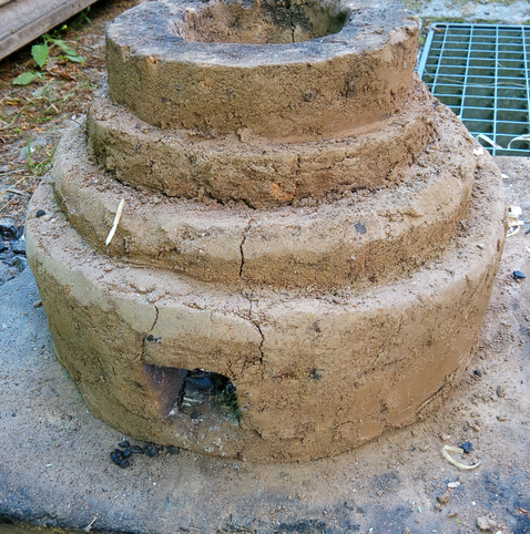 Ein kleiner Lehmofen etwa in Form und Größe einer Hochzeitstorte mit einem kleinen quadratischen Luftloch etwa in der Größe einer Dominopraline.