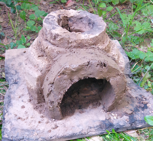 Derselbe Ofen, aber jetzt mit einem überdimensioniert wirkenden Eingang, etwa groß wie ein Ofenrohr.