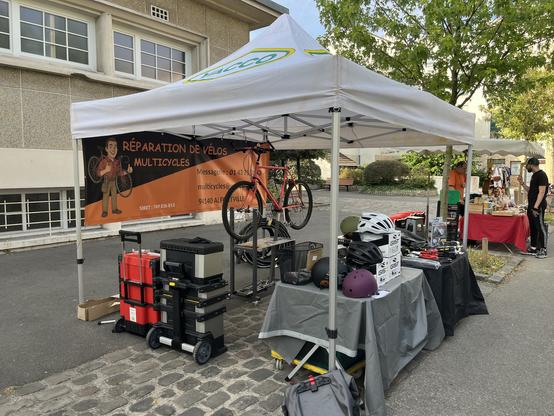 un stand d’entretien et réparation de vélos sur la place du marché du centre. sous un Barnum blanc des outils déployés et un VTT sur un pied d’atelier