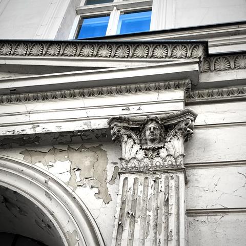 Ausschnitt aus einer Gründerzeitfassade, von der der Putz abbröckelt.