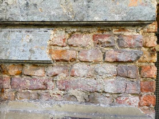 Backsteinmauer, bei der klassizistische Putz abbröckelt.