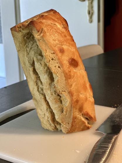 A loaf of bread is standing upright on a cutting board next to a knife.