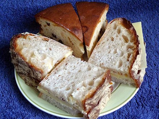 Small plate with a cheese and pickle sandwich made of two slices of the sourdough baked on Wednesday, cut into three parts, showing very open white crumb and a good rough brown crust.  Accompanied by the last two slices of a raisin cake made last weekend.
