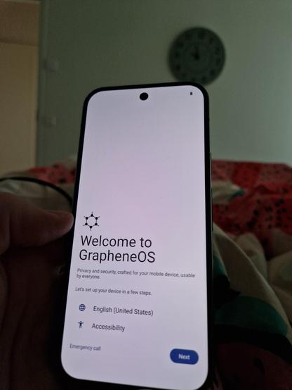 Puhelimen aloitusnäyttö jossa lukee "Welcome to GrapheneOS" . Kuva sängyssä maaten.
