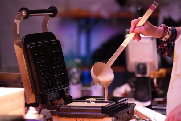 Waffelteig wird mit einer Kelle ins Waffeleisen gegeben