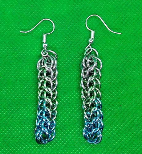 Earrings made in chainmail.
Starting at blue base, fading through green to silver tops.
Silver ear loops.
Green fabric  backdrop