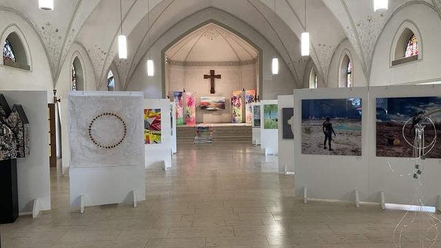 A bright church room. Instead of pews, there are partitions on which works of art are hung