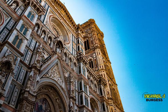 Dramatic upward view of Florence Cathedral’s ornate multicolored marble façade and adjacent Giotto’s bell tower set against a clear blue sky.