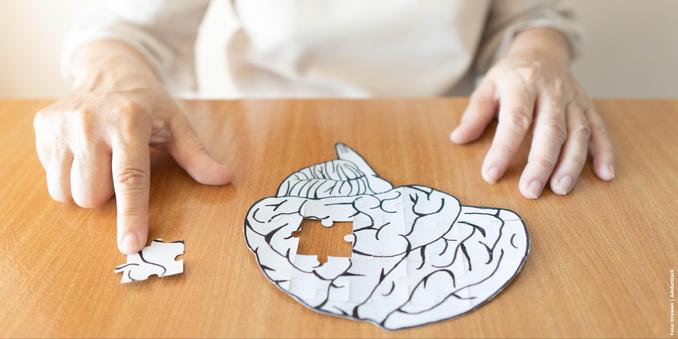 Eine Hand zeigt auf ein Puzzlestück, das fehlt, um ein Gehirn-Puzzle auf einem Holztisch zu vervollständigen.