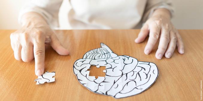 Hands placing a missing puzzle piece into a brain-shaped puzzle on a wooden table.