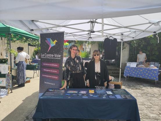 Un stand de La Contre-Voie avec un kakémono et des affiches. Deux personnes se tiennent derrière le stand.