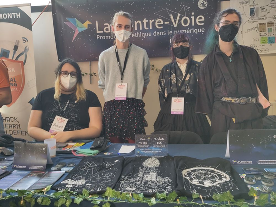 Quatre personnes de notre association devant une table recouverte d’une nappe et de nombreux goodies (tee-shirts, flyers, autocollants…). Au fond, une bâche affichant « La Contre-Voie − Promouvoir l’éthique dans le numérique ».