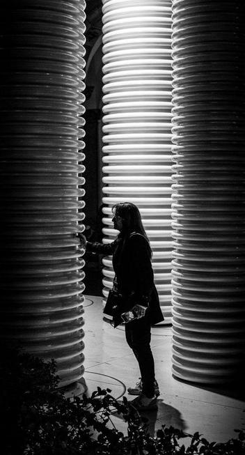A woman touches some kind of design installation at night. The installation is made of three tall cylinders with corrugated surface.