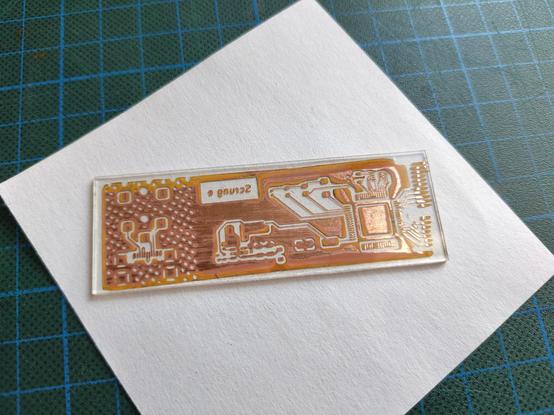 A photo of the back side of the PCB, showing the glue layer (or what's left of it) through the glass. There is a lot of corrosion on the back side and a lot of the glue layer has been stained by the copper chloride etchant.