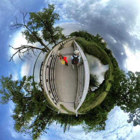 One of a series of photographs in which two people are pictured hiking, biking, and kayaking throughout a beautiful and verdant state park in central Minnesota under cloudy blue late-summer skies.