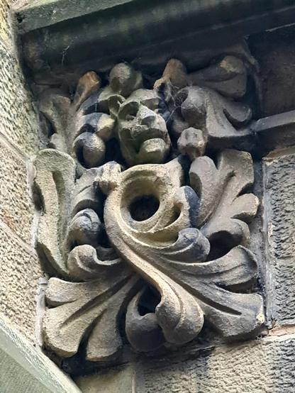 A decorative architectural sculpture with a big cat peeking out from some foliage.