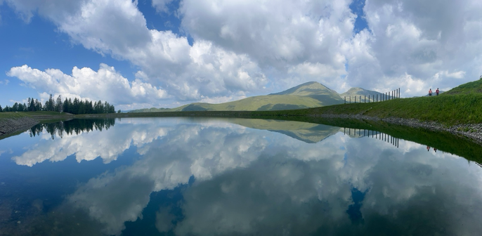 Bergpanorama mit grünen Hügeln und bewölktem Himmel, herrlich im Wasser gespiegelt in einem Berg Speichersee