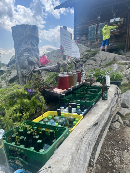 Wassertrog vor der hölzernen Almhütte mit 6 Getränkekisten drinnen und weiteren Säften zur Kühlung mit Bergwasser