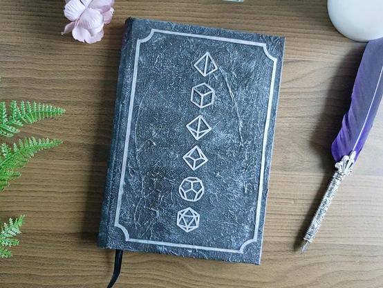 A5 Notebook in silver tones with six DnD dice in the middle top to bottom.