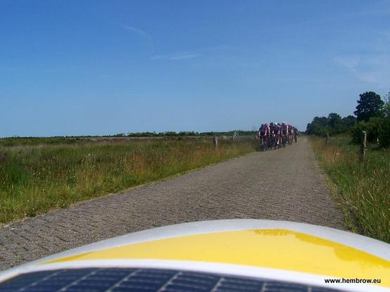 Riding along a narrow country rode against the flow (but it's wide enough that this isn't a problem). A group of racing cyclists ahead.