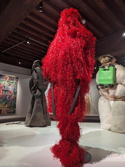 Sorte de mannequin recouvert d'un costume en plastique effiloché rouge brillant, et tenant deux sabres