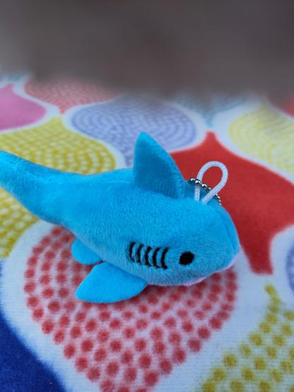 Tiny plushie shark with a teddy paw covering half of the lens.