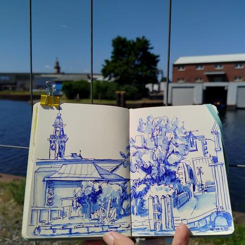 Sketchbook in front of the scenery. City harbor Dortmund with historic 'Hafenamt' drawn with blue ink.
