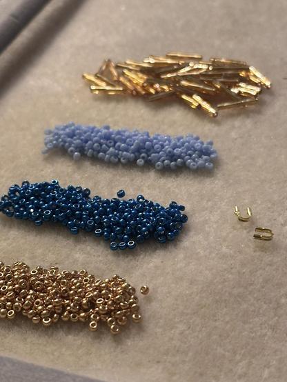 Piles of seed beads in blue and gold lined up on a cream colored bead mat