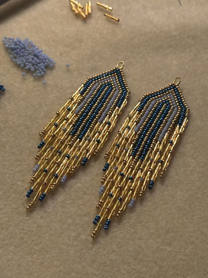 A pair of beaded fringe earrings in blue and gold on a bead mat