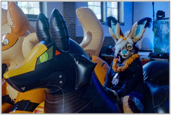 A bunny fursuiter with giant ears sitting pretty on a big inglatable mecha looking fox