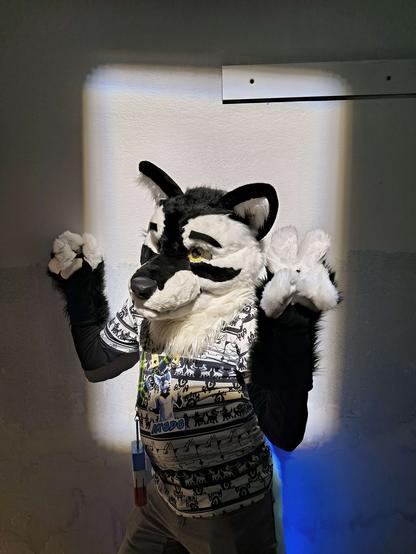 Ikodo in partial fursuit posing and giving the peace sign in an artistically placed spotlight at the Geogia Aquarium