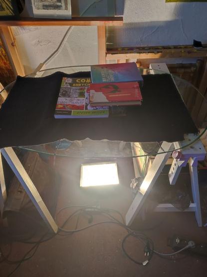 you can see a glass table with a very bright light underneath. On the table is black molton fabric and some books stacked on it. What can't be seen directly is the silkscreen which is hidden from the molton.