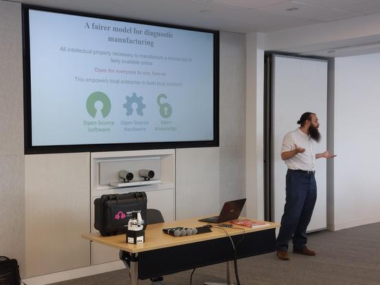 A speaker standing in front of a whiteboard with a slide titled "A fairer model for diagnostic manufacturing".