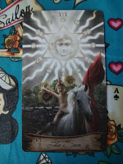 Card from the Heaven and Earth Tarot deck.
The Sun-XIX. 
A child rides a white horse, holding a red banner on the left hand. Sun shining brightly behind them over some sunflowers.