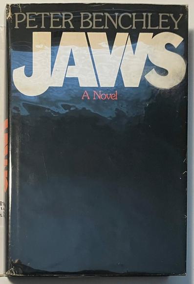 This is the original dust jacket for the first edition of Jaws, a novel by Peter Benchley, published in 1974 by Doubleday. The iconic cover features:

    The author's name “PETER BENCHLEY” in a large serif font at the top.

    The word JAWS in massive, bold, block letters dominating the upper half, with a gradient shading suggesting depth in the ocean.

    The subtitle “A Novel” in red, smaller serif font below the title.

    A dark, mostly black lower half symbolizing the ominous ocean depths, evoking a sense of suspense and fear—very fitting for the story’s theme.