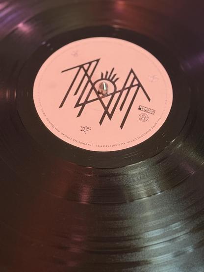 The A side of “Sundowning” by Sleep Token. It’s a black vinyl record with a white label and the logo for the band in black.