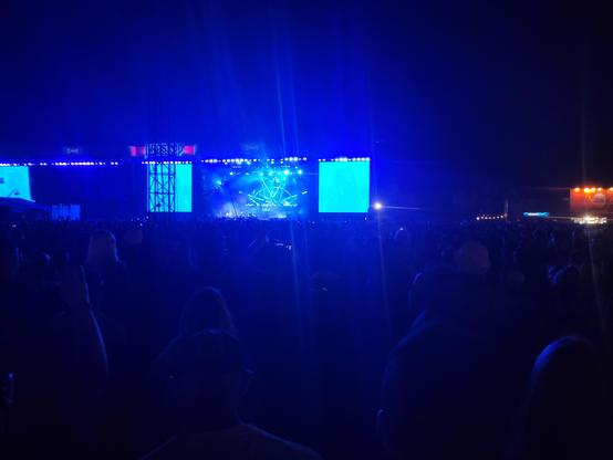 Podium waarop Slipknot op Graspop 2025 speelt vanaf een afstand. Het podium wordt blauw verlicht. Het is te donker om het publiek te zien.