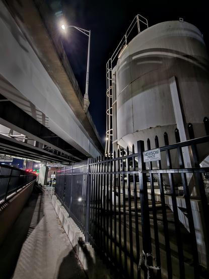 Dark, shadowy view of a fenced in footpath beneath a bridge overpass.