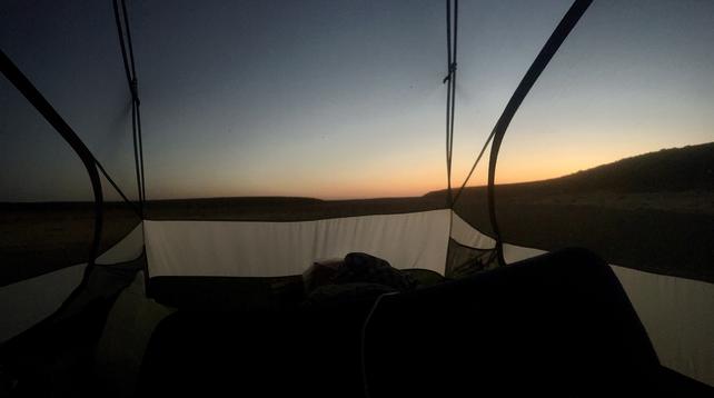 The sun just about to peak over the horizon as visible from inside a tent with no rain fly mounted, just a netting top.