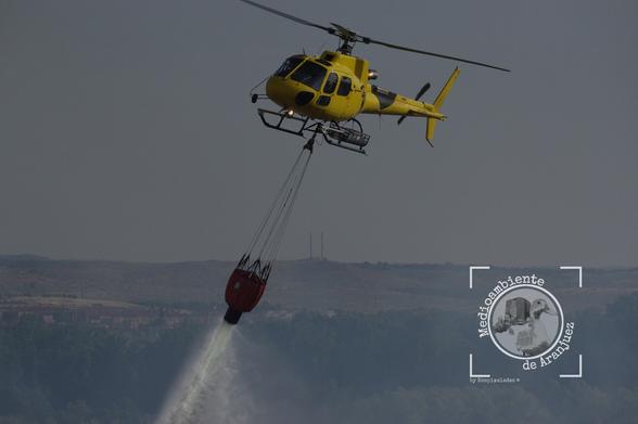 helicóptero amarillo realizando una descarga de agua sobre un incendio