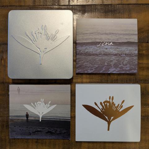 Four components of the Ixora packaging laid out in a grid. Metal case with embossed ixora silhouette, "ixora" handwriting over a photo of low breaking waves on a digipak, white ixora silhouette over a double exposed beach photo on a digipak, and reflective gold ixora silhouette on a white slipcover.